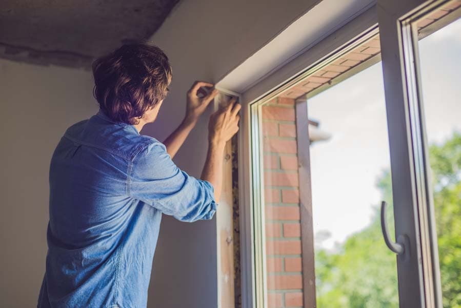This is a picture of a man in a blue shirt does window installation at home.