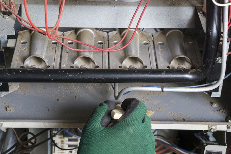 A maintenance worker servicing a furnace with green gloves.