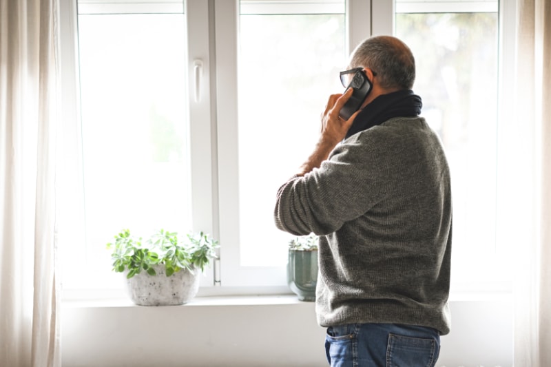 Why Won’t My Furnace Stop Running? Man on phone looking out window.