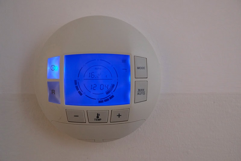 Photo of a digital thermostat mounted on a wall with a blue light.